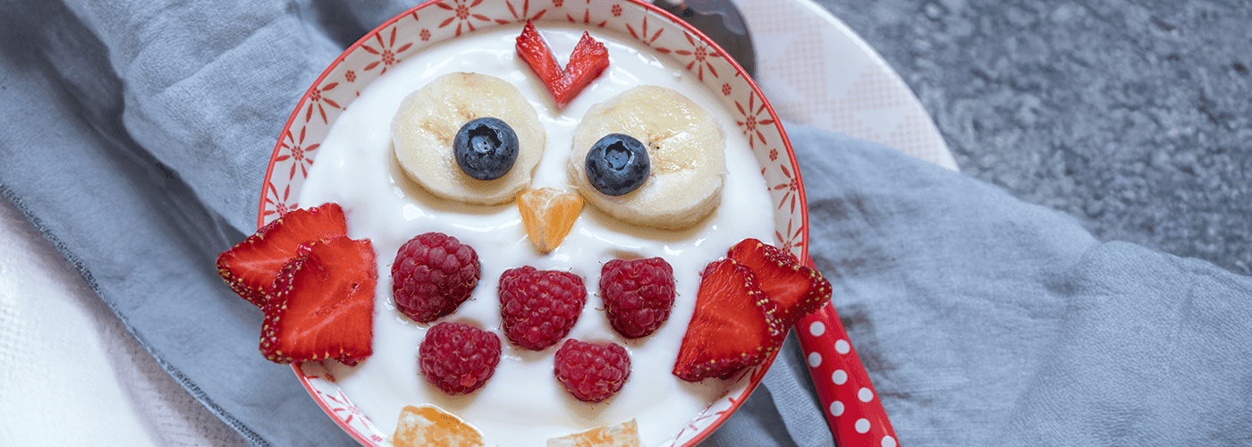 A bowl of yogurt with fruit on top, including banana, blueberries, strawberries and oranges.